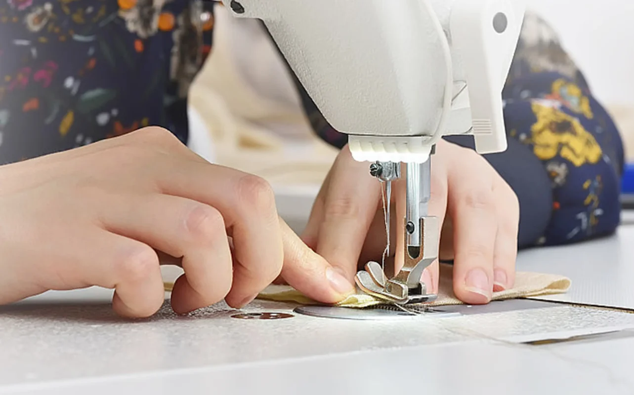 Close - up of hands skillfully operating a sewing machine, showcasing the craftsmanship of top lingerie manufacturers. Ideal for suppliers of womens lingerie, highlighting the precision and quality in creating the best - in - class products.