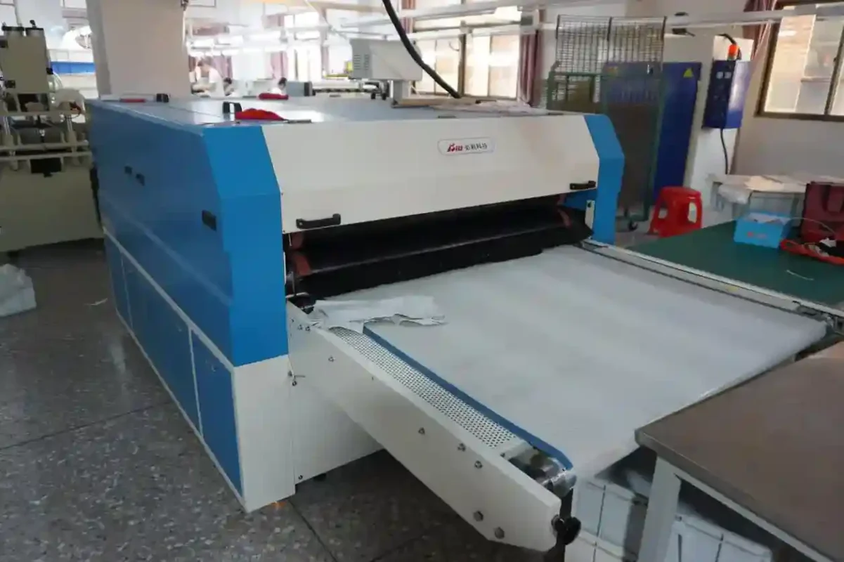 A large industrial machine in a factory environment with fabric on its conveyor belt representing the equipment utilized by underwear suppliers and vendors in production processes