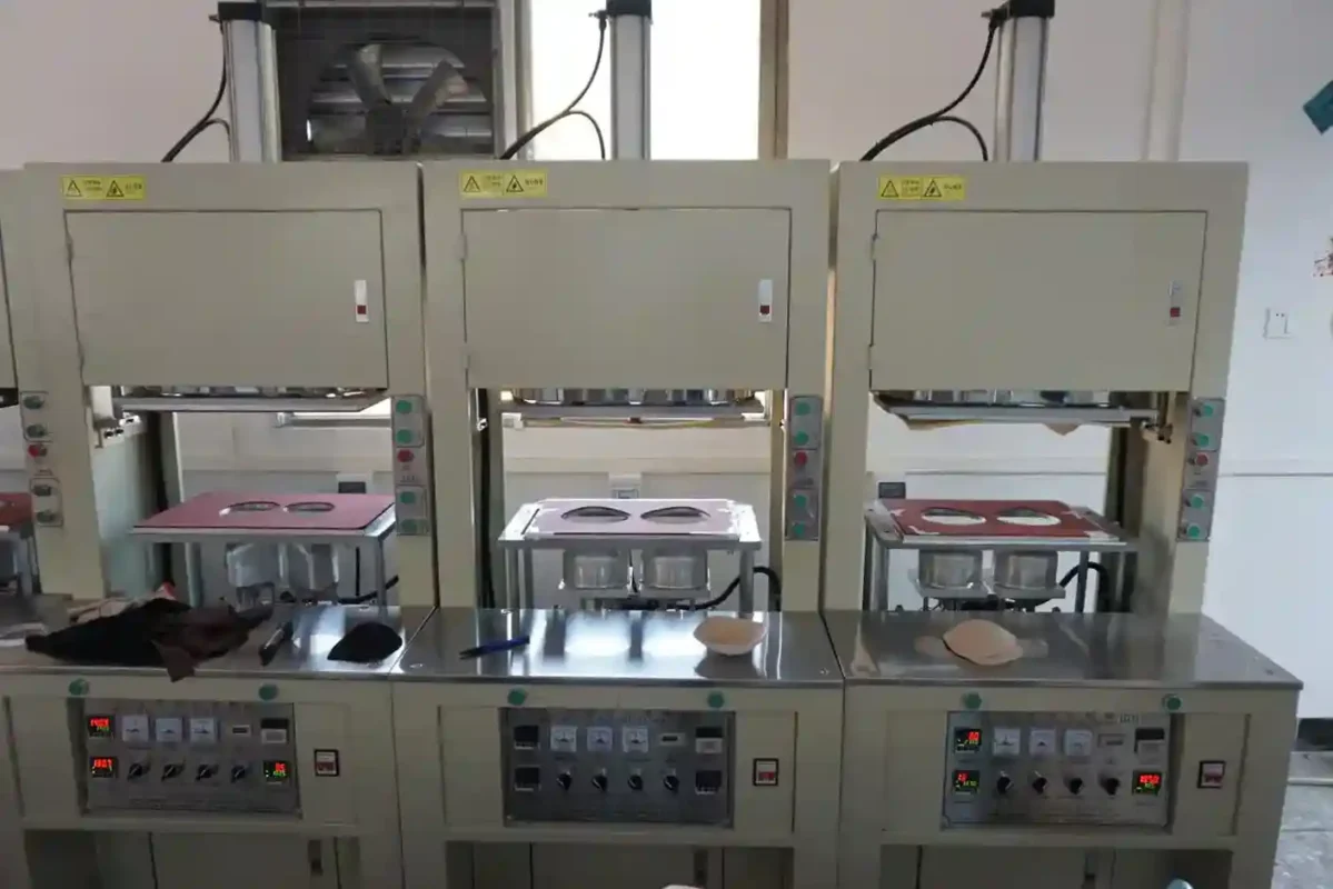 Three industrial pressing machines in a factory setting with bra components on the work surfaces demonstrating the equipment used by underwear suppliers and vendors in manufacturing processes