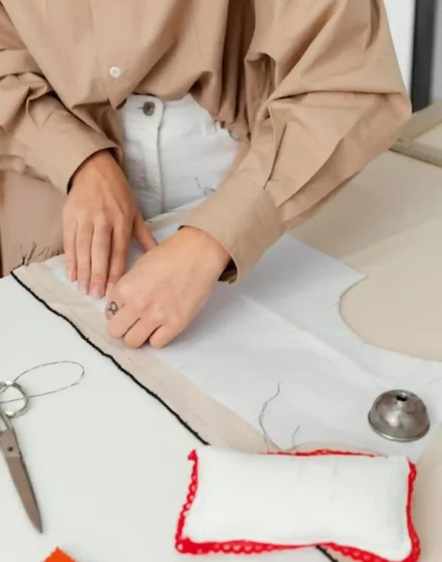 Our Cut and Sew Underwear Manufacturing Service02 zoralinkcom A person in a tan shirt working on a white fabric pattern with sewing tools like scissors and a thimble nearby demonstrating the cut and sew process for underwear or garment making