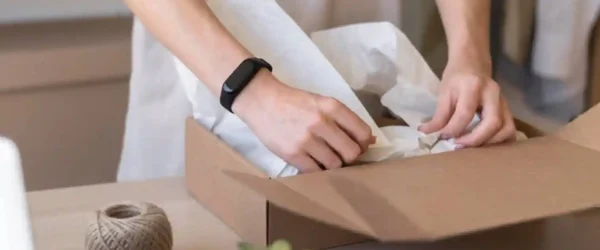 Our Journey Towards EcoFriendly Biodegradable Recyclable Packaging04 zoralinkcom A person packing items into a cardboard box with sustainable wrapping paper alongside a ball of twine exemplifying our commitment to supply chain sustainability