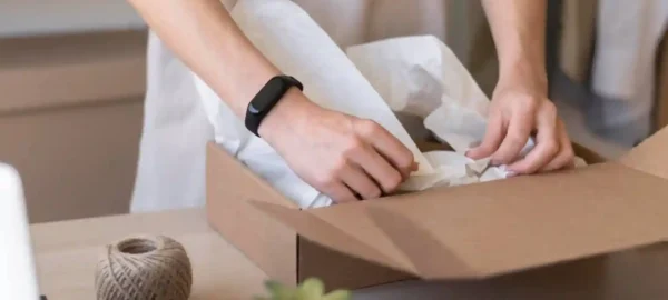 A person packing items into a cardboard box with sustainable wrapping paper, alongside a ball of twine, exemplifying our commitment to supply chain sustainability.