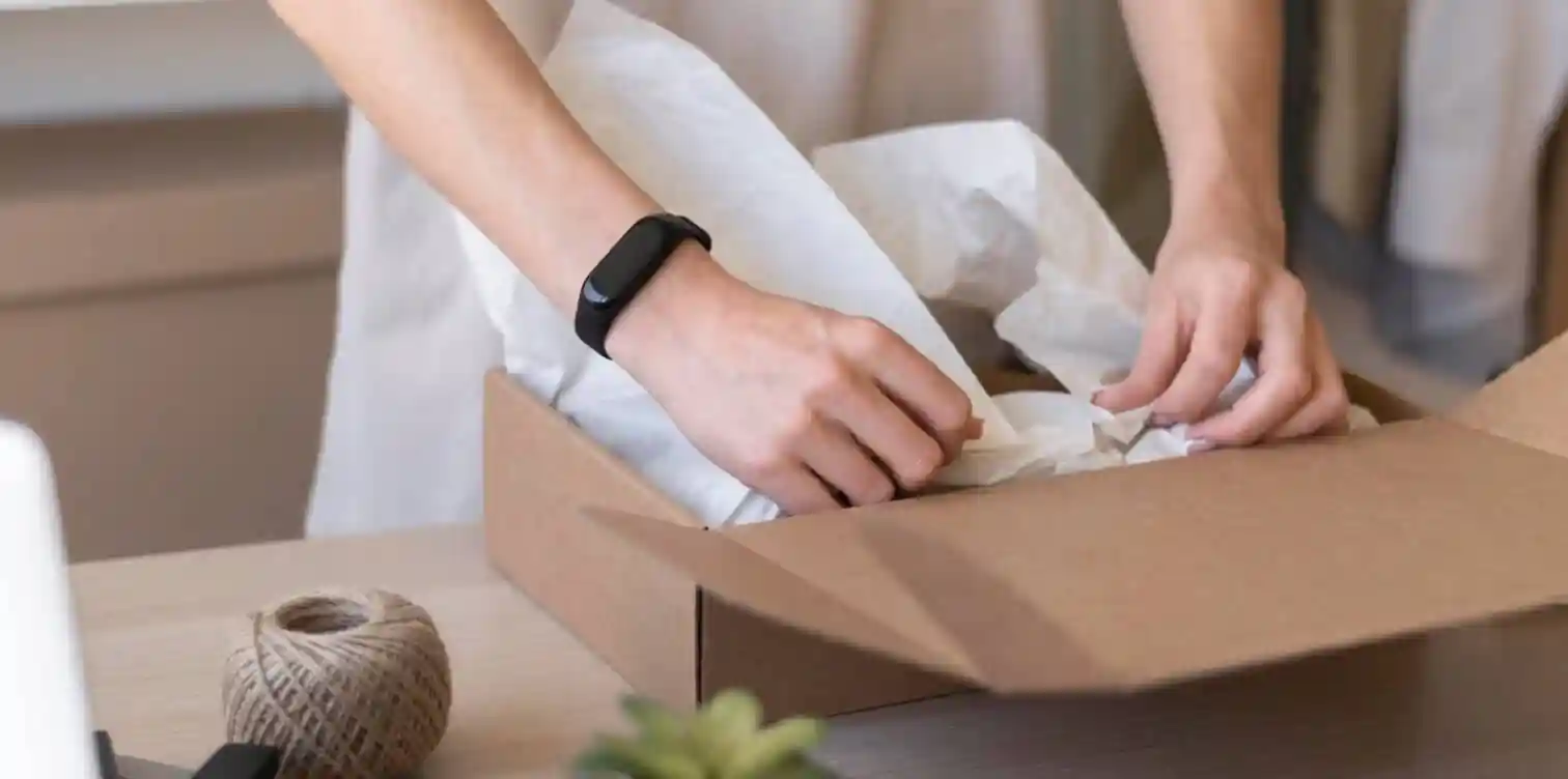 Our Journey Towards EcoFriendly Biodegradable Recyclable Packaging04 zoralinkcom A person packing items into a cardboard box with sustainable wrapping paper alongside a ball of twine exemplifying our commitment to supply chain sustainability