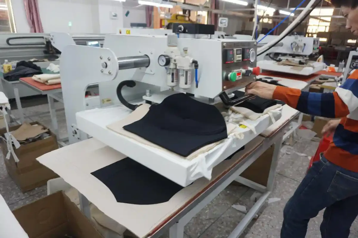 A worker operating industrial machinery on black fabric pieces in a factory environment reflecting the production efforts of underwear suppliers and vendors