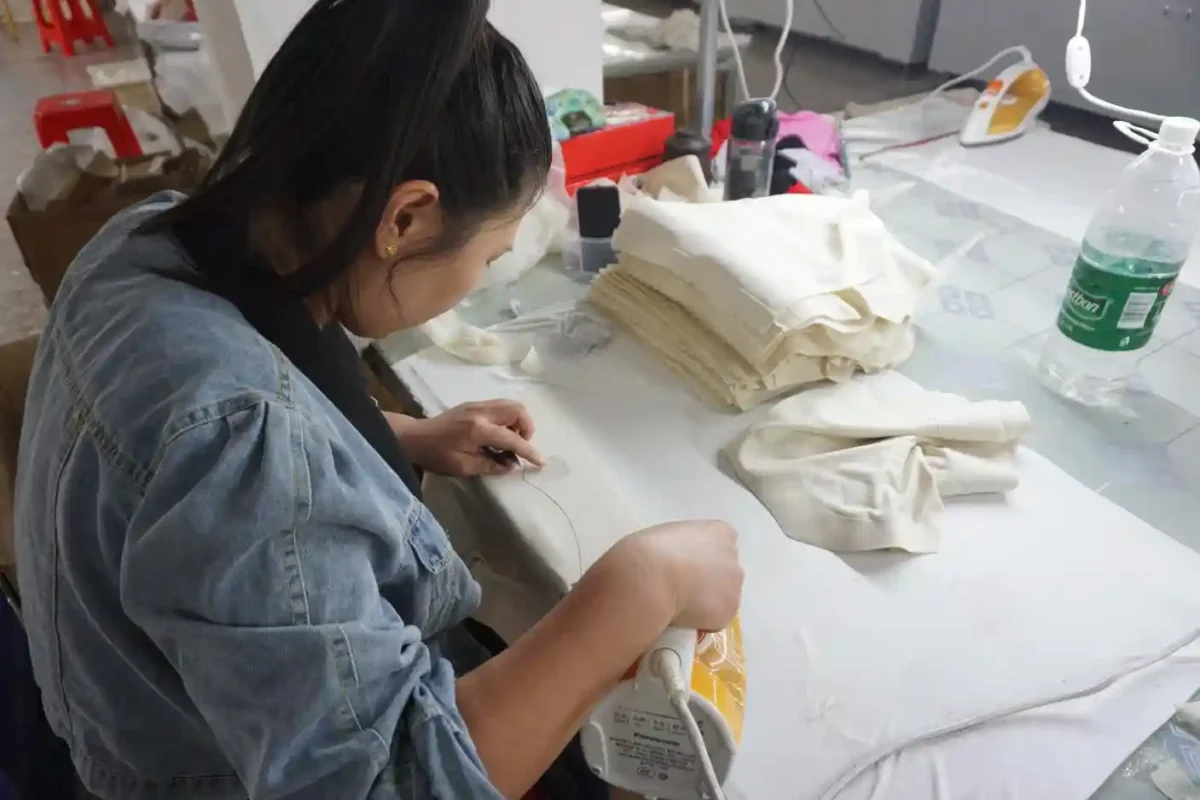 A worker in a denim jacket meticulously working on fabric surrounded by stacks of material embodying the craftsmanship of underwear suppliers and vendors