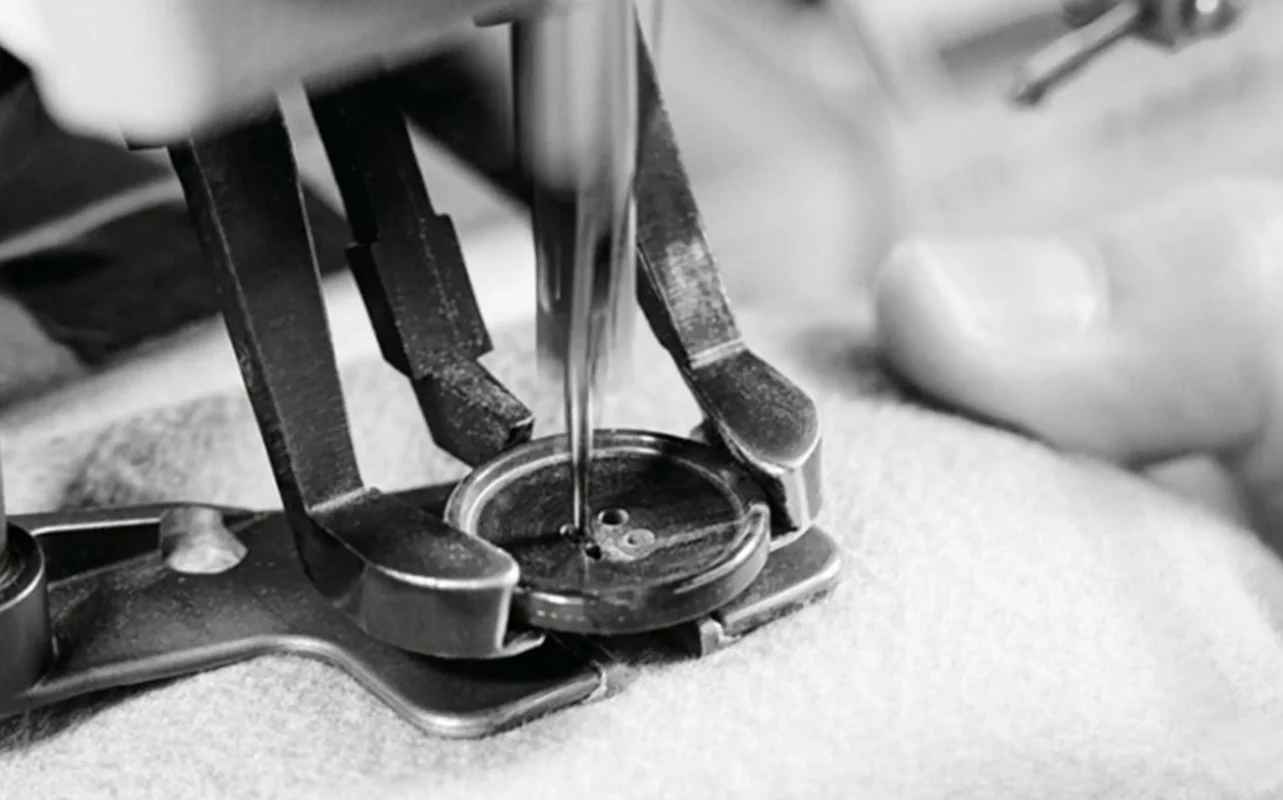 Close - up of a sewing machine attaching a button to fabric, representing meticulous craftsmanship in lingerie manufacturing. Symbolizes a lingerie manufacturer's commitment to quality, appealing to clients seeking wholesale womens lingerie with attention to detail.